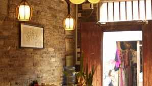 Una habitación con pared de ladrillo, lámparas de mimbre colgantes, un cuadro enmarcado y una puerta de madera que da a una tienda.