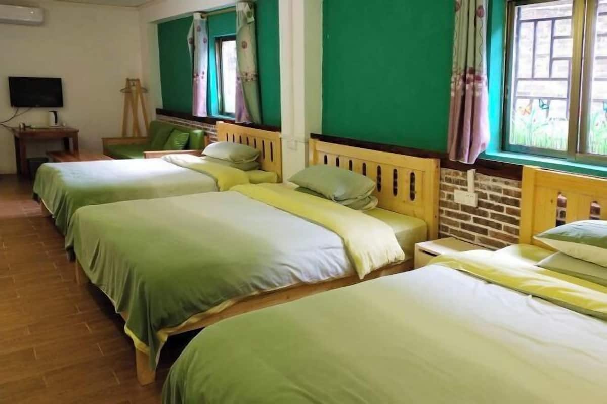 A room with three beds, a television, a wooden nightstand, and a brick wall.