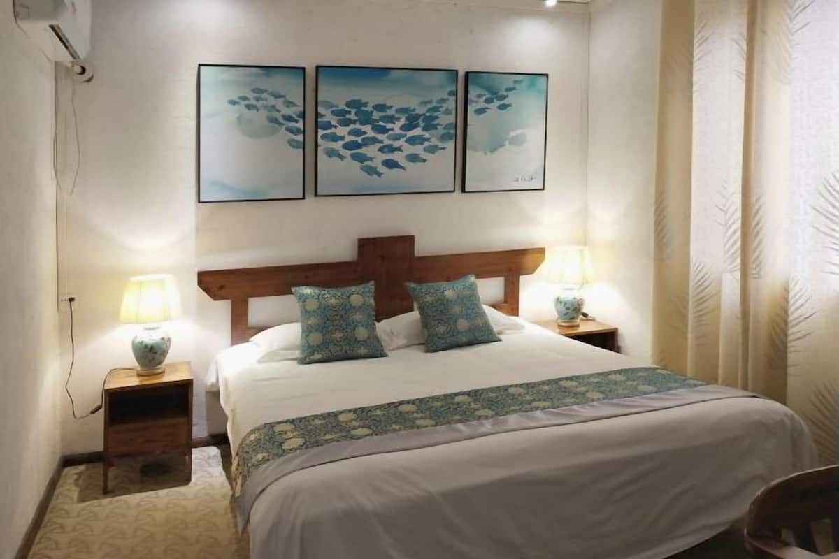 A bedroom with a wooden headboard, a bed with white bedding, two matching lamps, and three framed artworks on the wall.