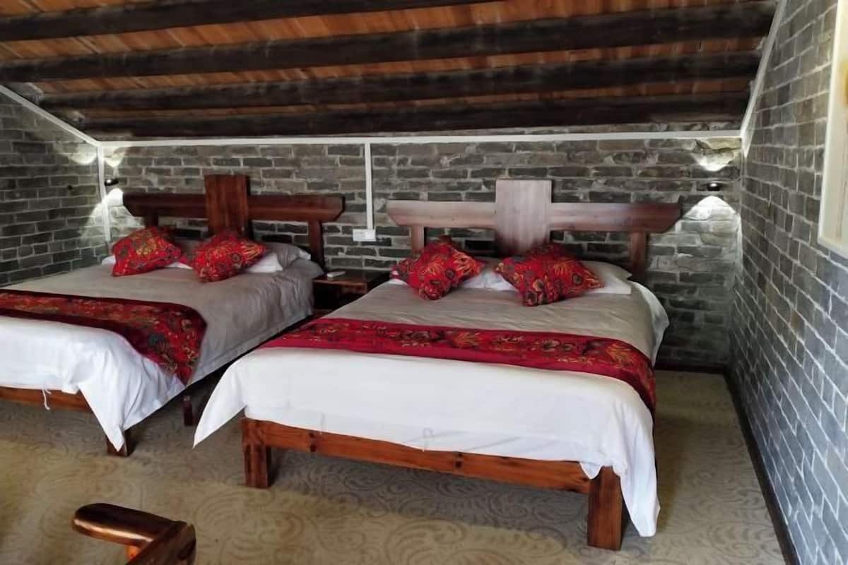 Two wooden beds with white and red bedding, a stone wall, and a wooden ceiling.