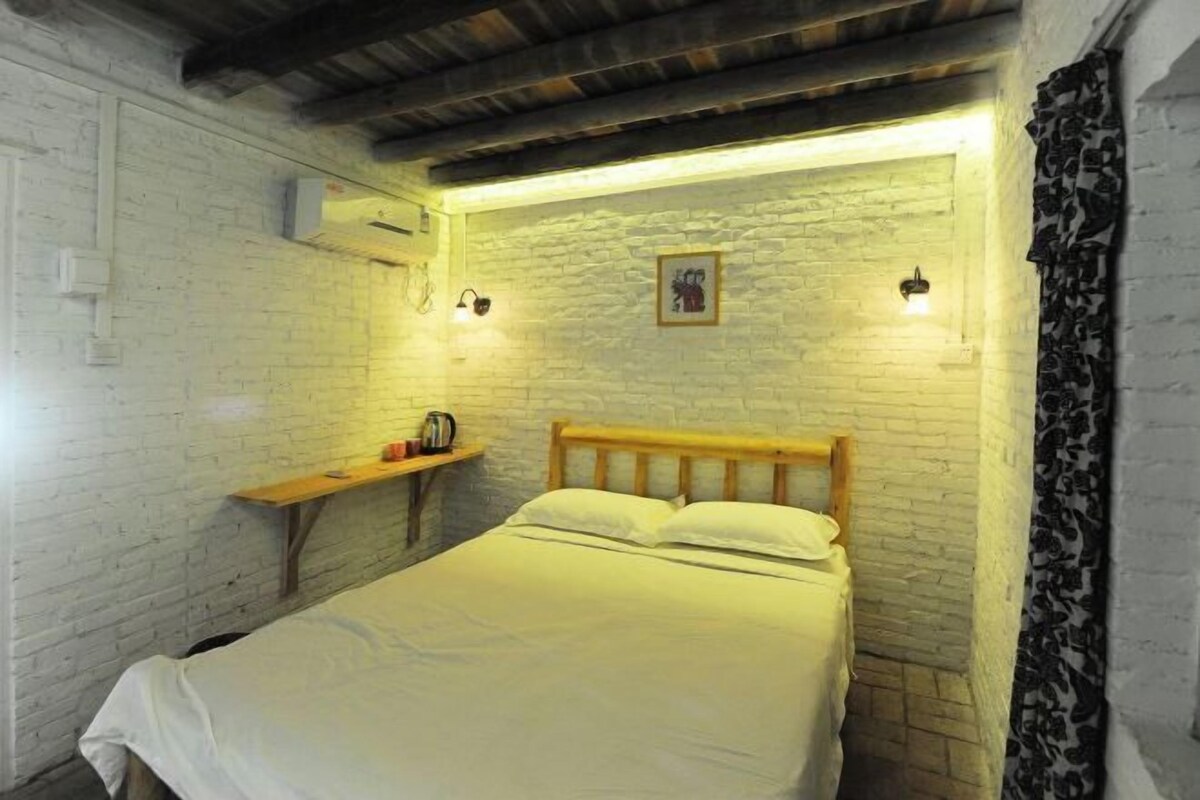 A single bed with a wooden headboard in a room with white brick walls and exposed wooden beams.