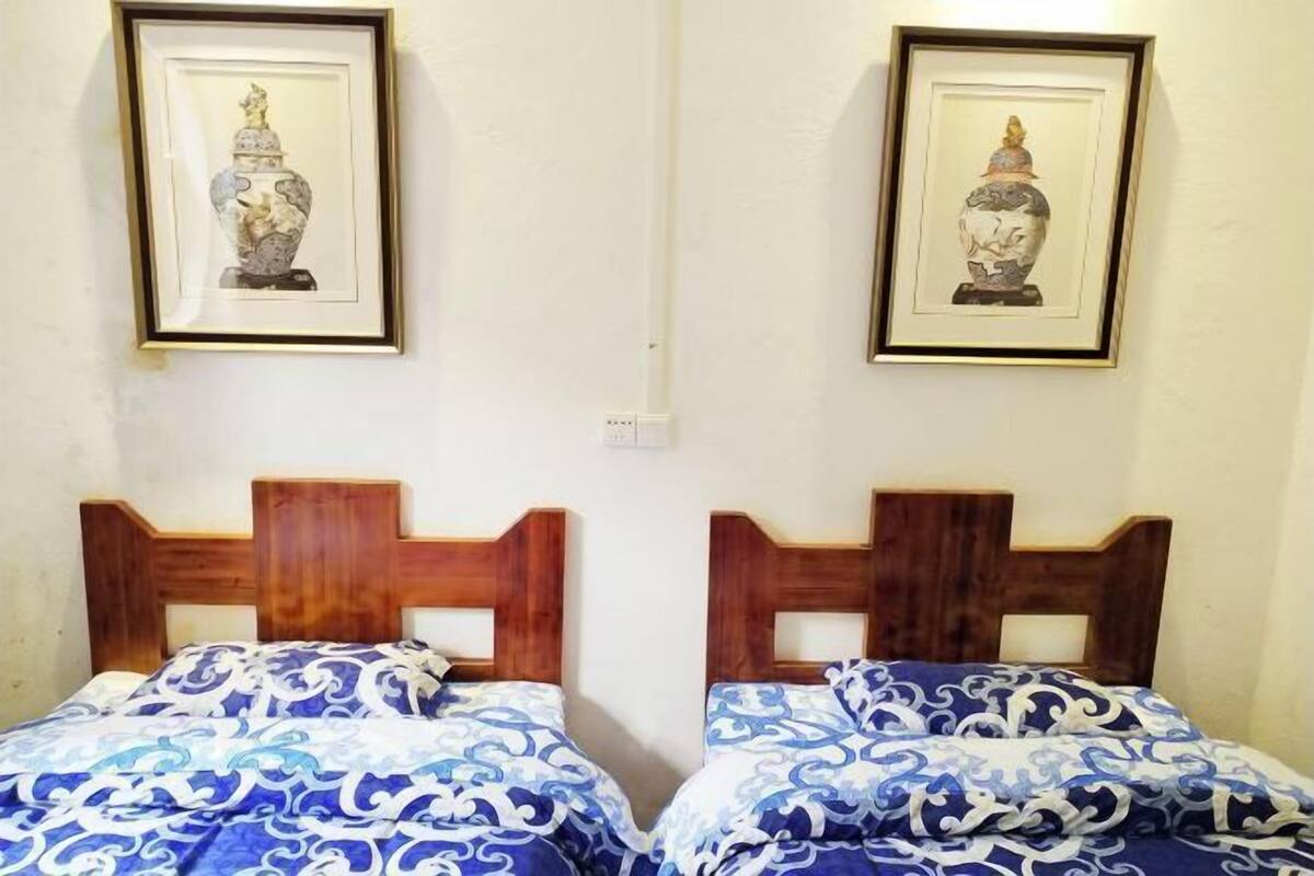 A room with two beds, each with a wooden headboard and blue patterned bedding. There are two framed artworks on the wall above the beds.