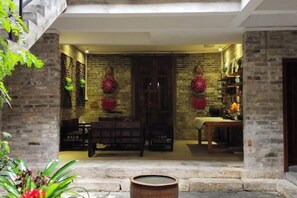 A brick-walled interior with a wooden table and chairs, a large door, and a stone planter with red flowers. - Huangyao Guyaju Farm Inn (Zhaoping)