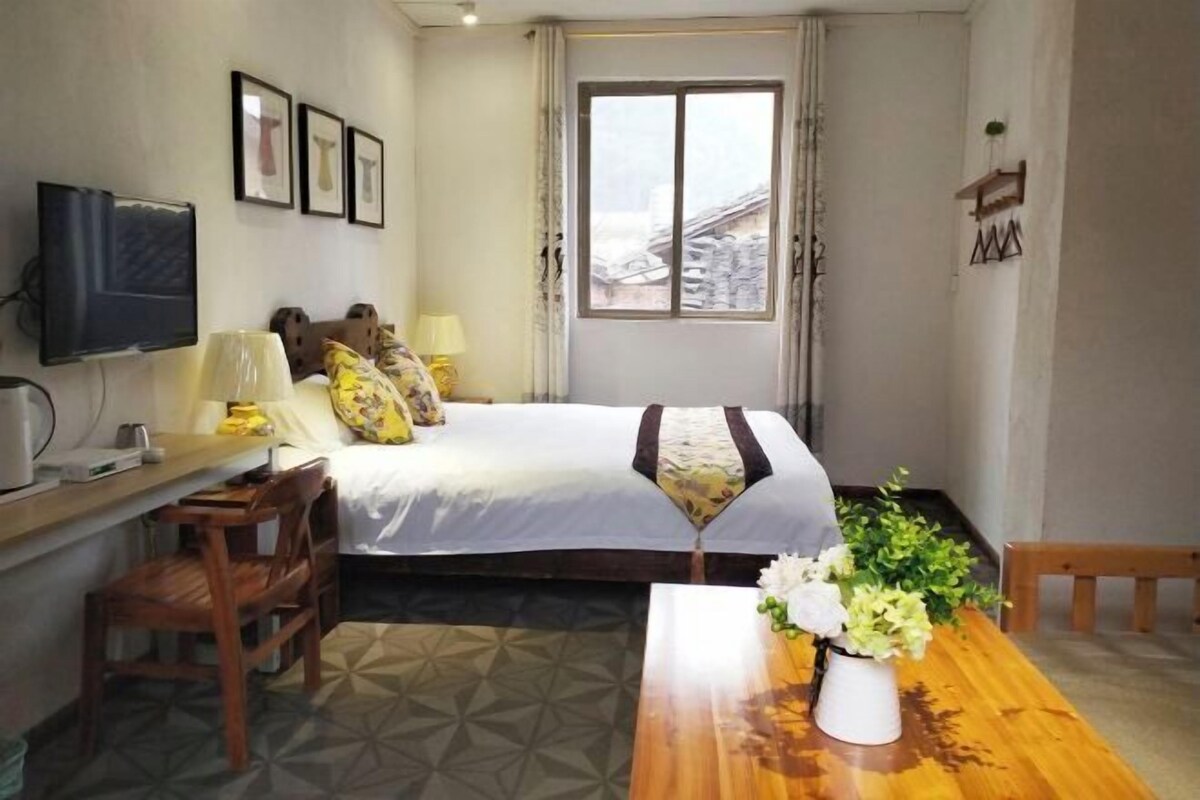 A hotel room with a bed, a desk, a chair, a TV, and a window with a view of buildings.