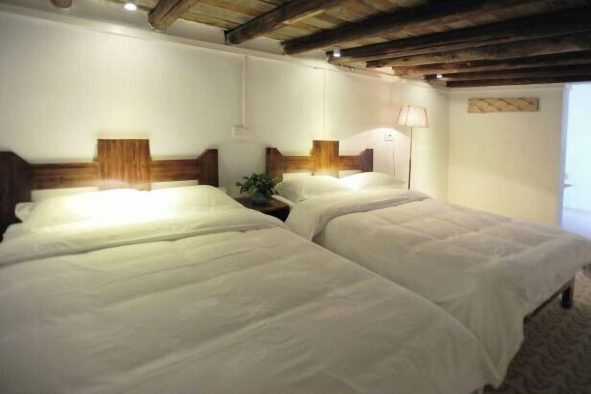 A room with two beds, wooden headboards, bedside lamps, and a door leading to another room.