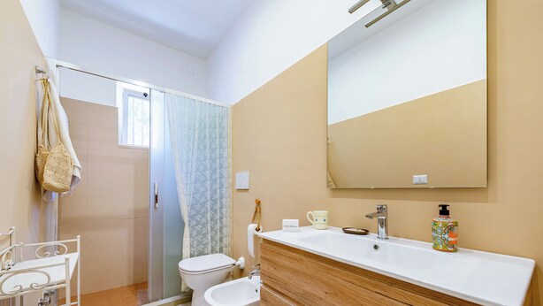 Ein Badezimmer mit Dusche, Toilette, Bidet, Waschtisch mit Spiegel und Waschbecken.
