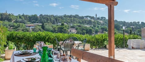 An outdoor dining area with a table set for four, overlooking a vineyard and hillside.