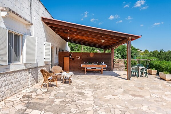 A covered outdoor patio with stone flooring, wicker furniture, and a wooden table. - Casa Vacanze Minare Selva di Fasano (Fasano)