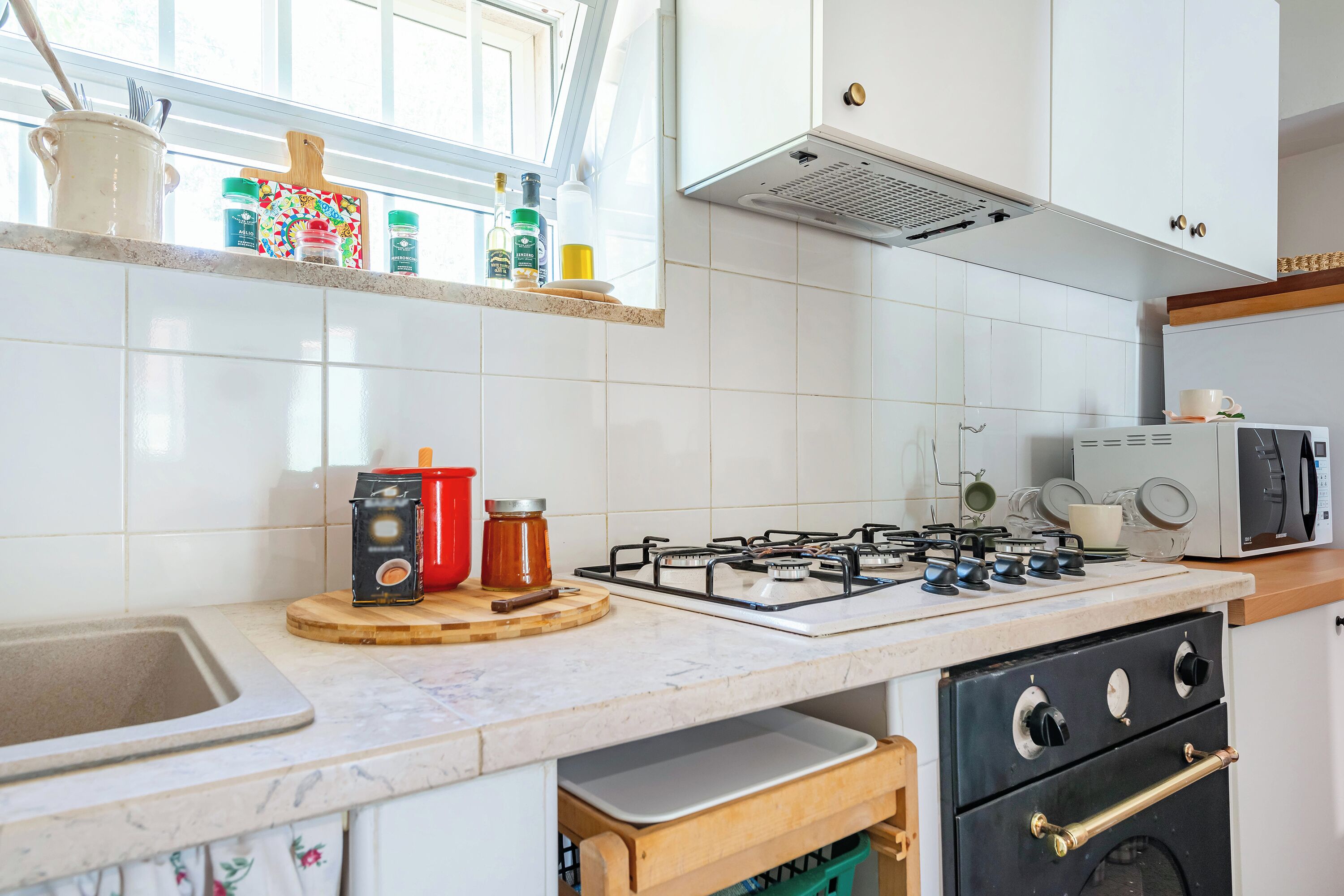 A kitchen with white tiles, a gas stove, a microwave, and a sink.