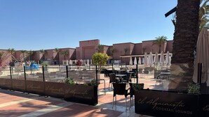 Een terras met tafels en stoelen, palmbomen en een gebouw op de achtergrond.