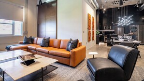 A modern living room with a sectional sofa, a black leather armchair, and a dining area with a table and chairs. - Wynwood Condo, Walk to Restaurants & Nightclubs! (Miami)