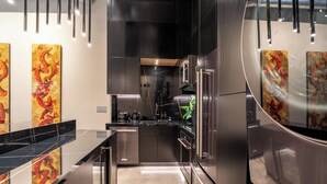 A modern kitchen with stainless steel appliances, black countertops, and abstract artwork on the walls. - Wynwood Condo, Walk to Restaurants & Nightclubs! (Miami)