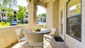 A covered outdoor seating area with a round table and four wicker chairs, a small potted plant, and a view of the street and buildings in the background. - 3 Mi to Tpc: Chic Condo w/ Pool Access & Grills (Scottsdale)