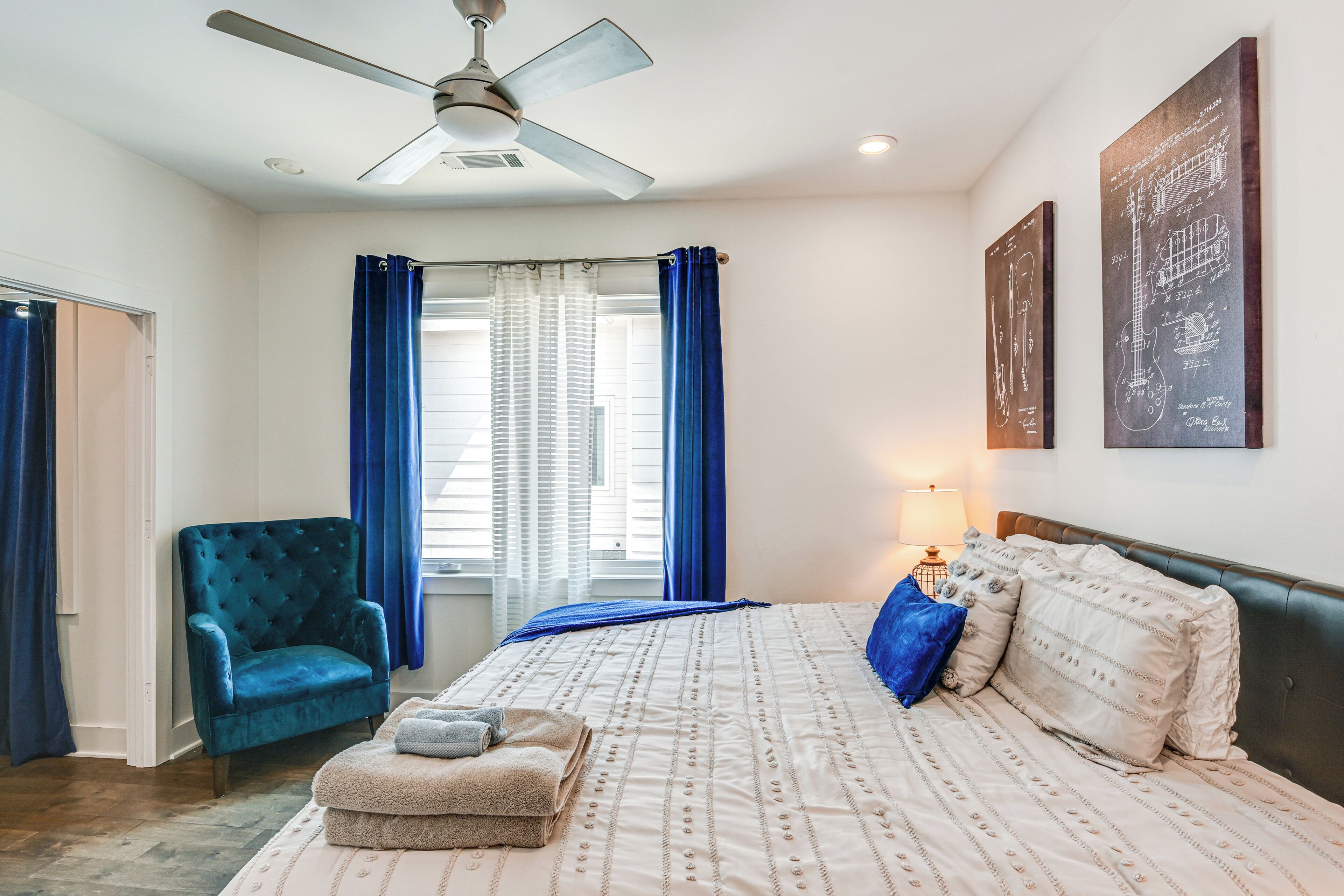 A bedroom with a bed, a chair, a ceiling fan, and curtains.