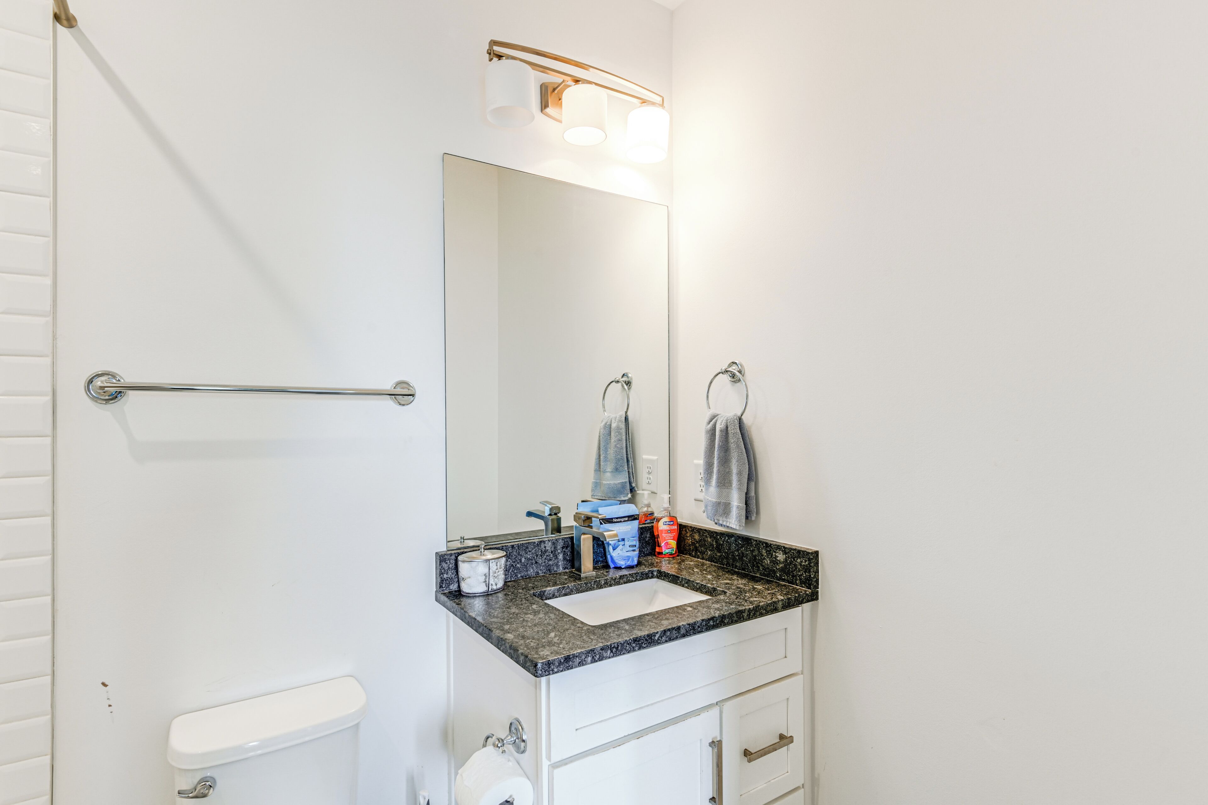 A bathroom with a white toilet, a sink with a granite countertop, a mirror, and a towel rack.