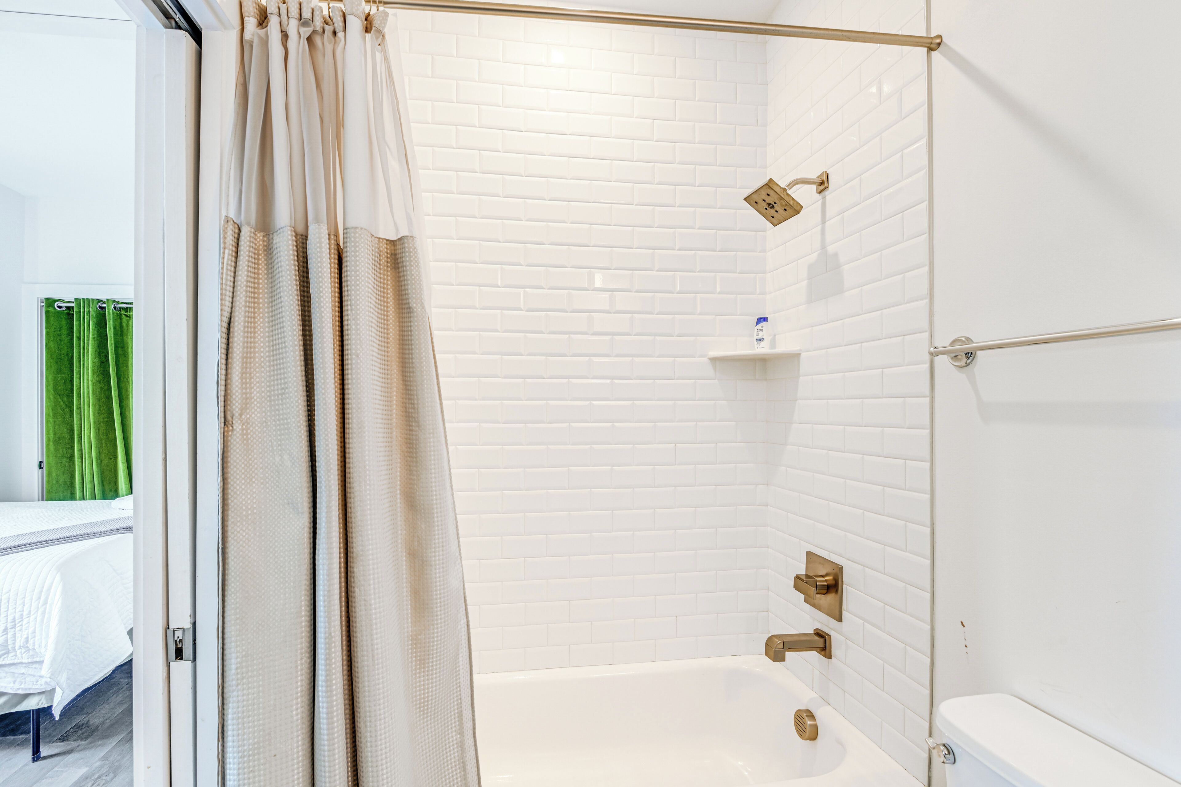 A modern bathroom with white subway tiles, a bathtub, a shower area, and a green curtain.