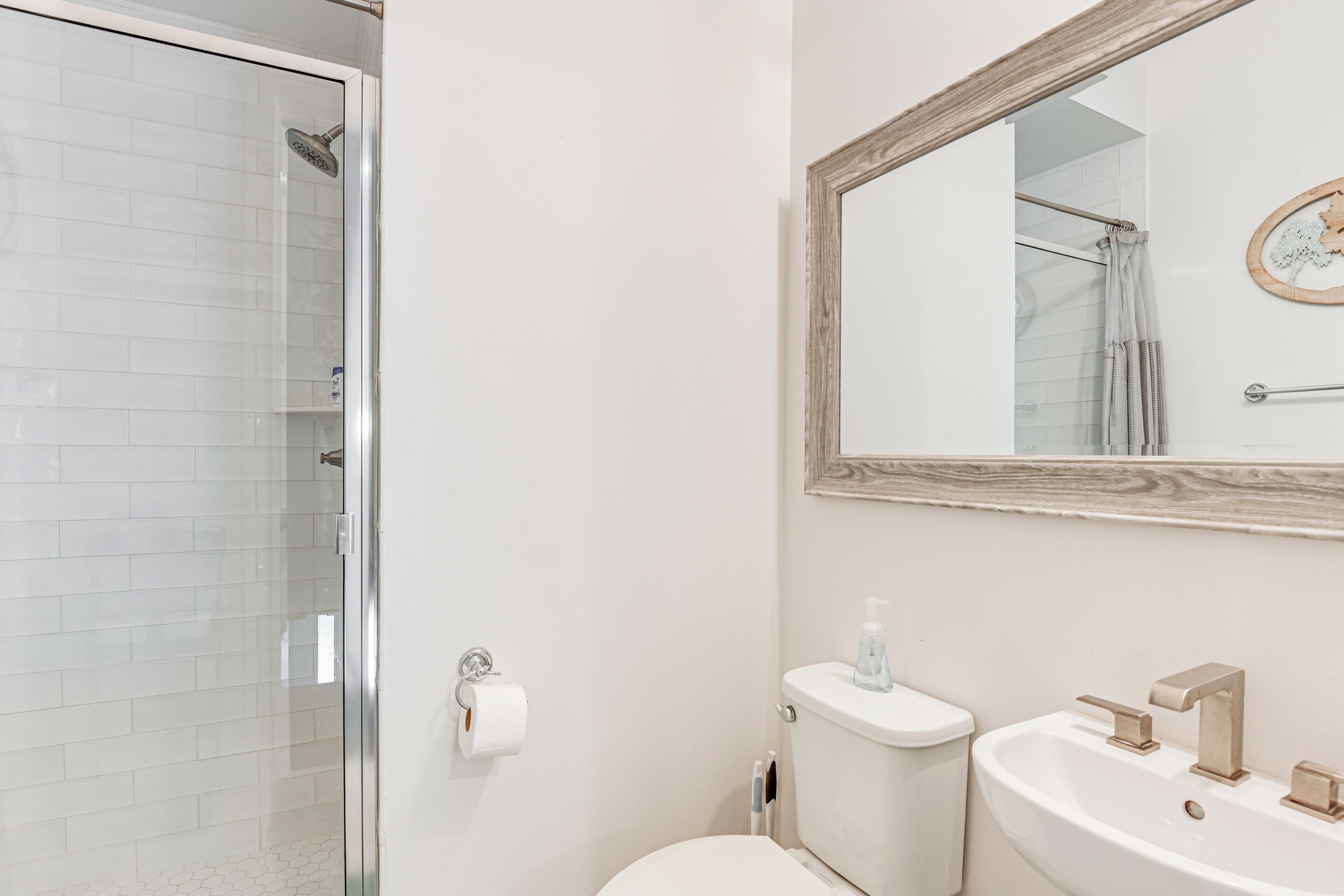 A bathroom with a glass shower enclosure, a toilet, and a sink with a mirror above it.