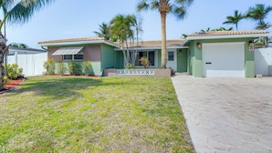 A two-story house with a green exterior, a tiled roof, and a front yard with grass and palm trees. - Pompano Beach Home w/ Pool & Dock ~ 4 Mi to Pier! (Pompano Beach)
