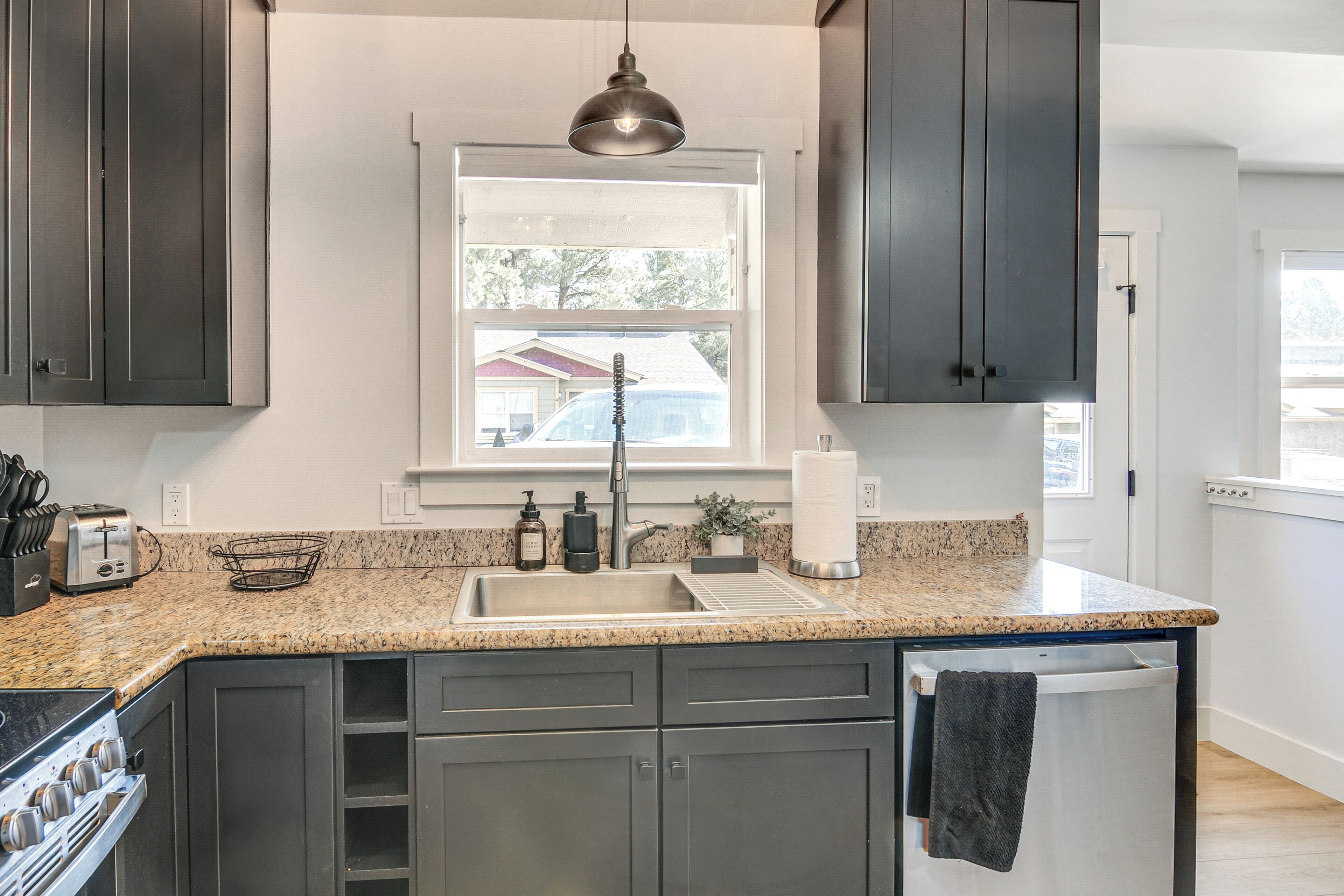 A modern kitchen with dark cabinets, a granite countertop, a built-in oven, a sink, and a window above the sink.
