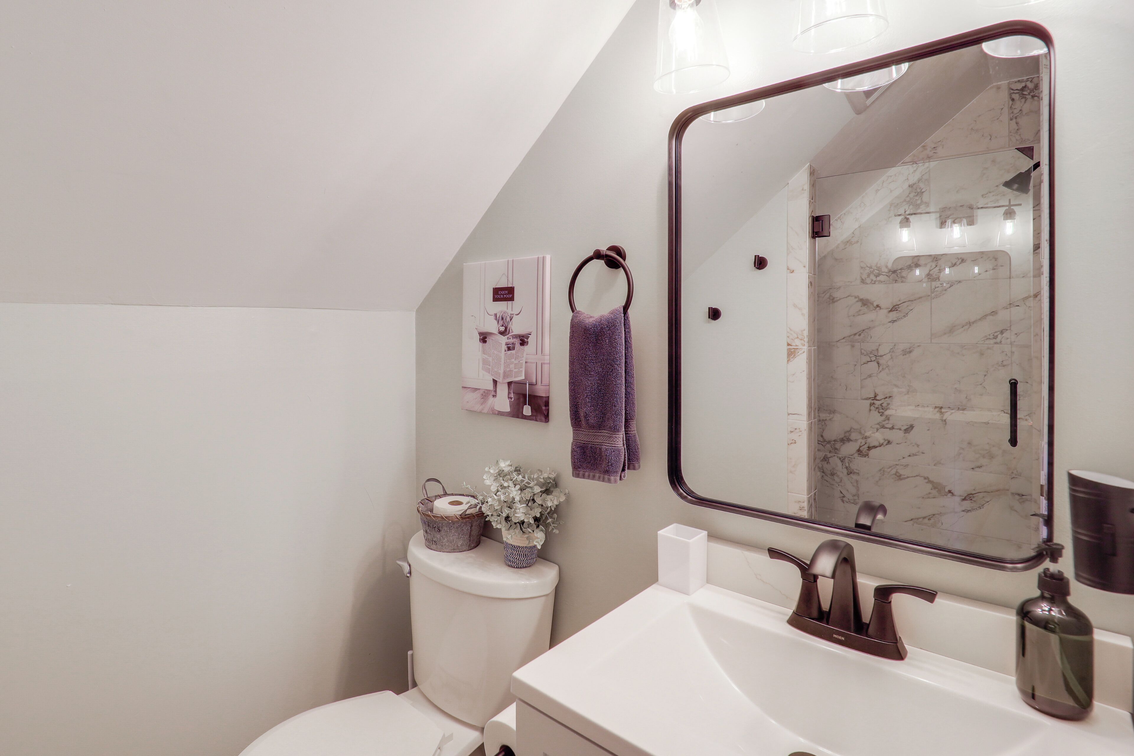 A modern bathroom with a white sink, a large mirror, and a marble shower wall.