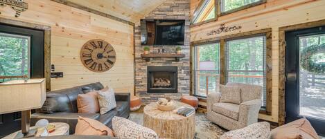 A cozy log cabin interior with a fireplace, leather sofas, and a large clock on the wall.