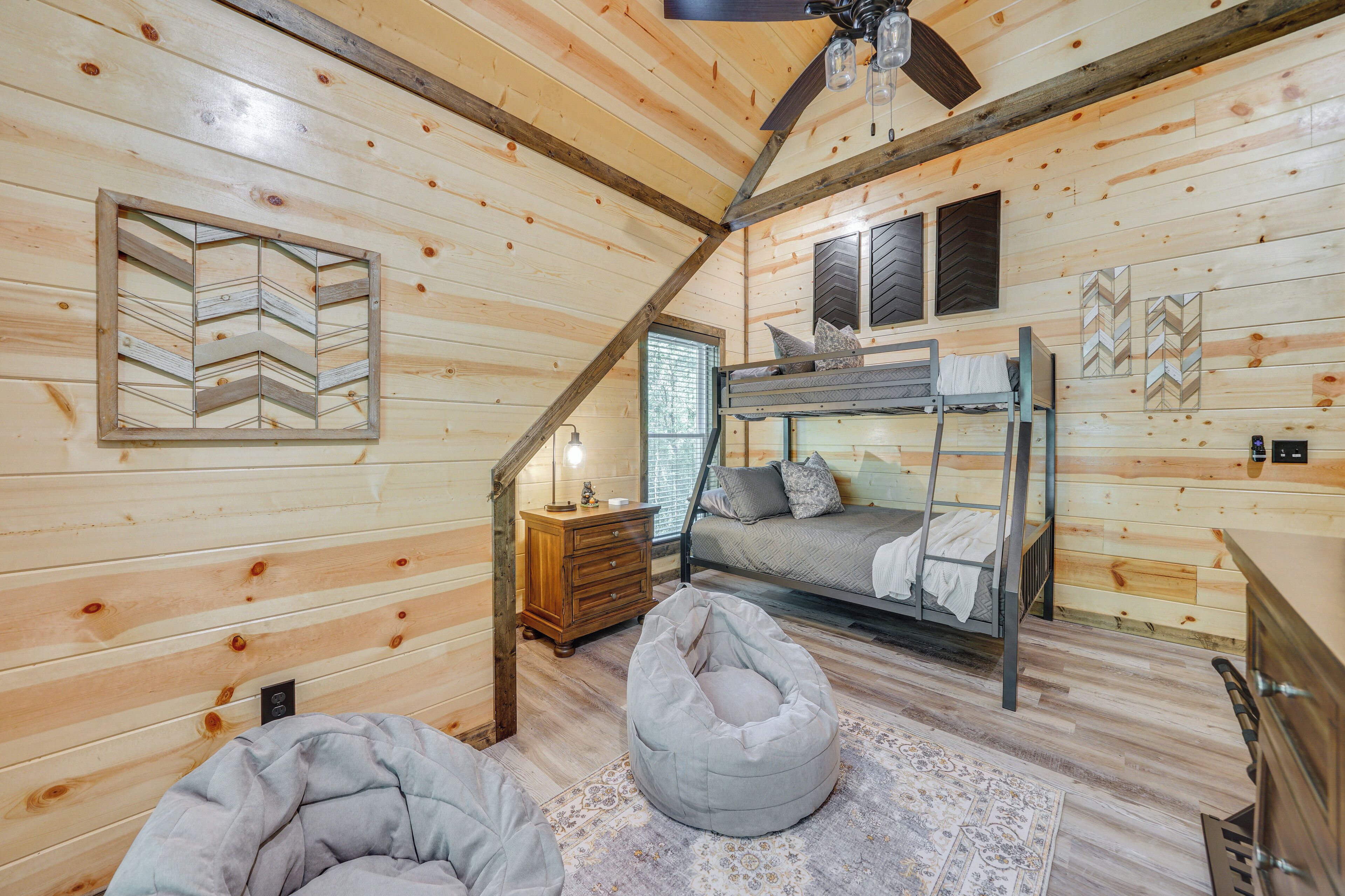 A cozy cabin interior with a loft bed, a lower bunk bed, a wooden dresser, and a bean bag chair.