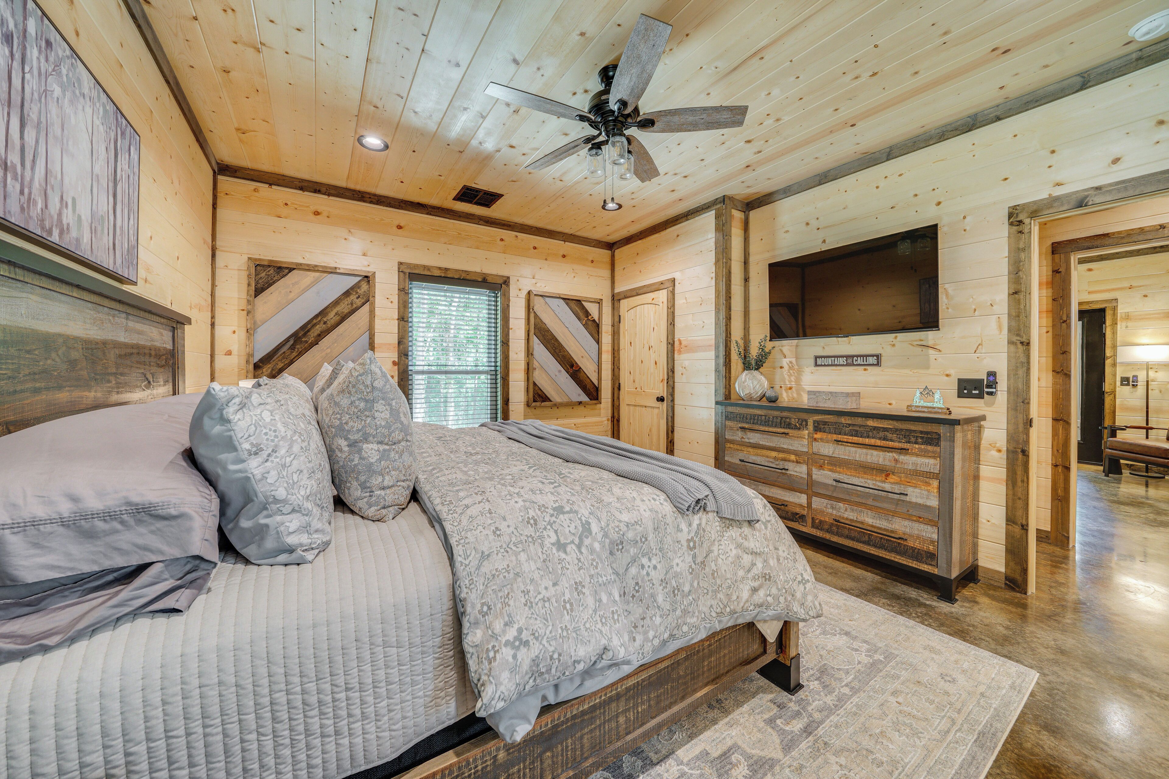 Une chambre à coucher avec un lit, un ventilateur de plafond, une commode et un téléviseur.