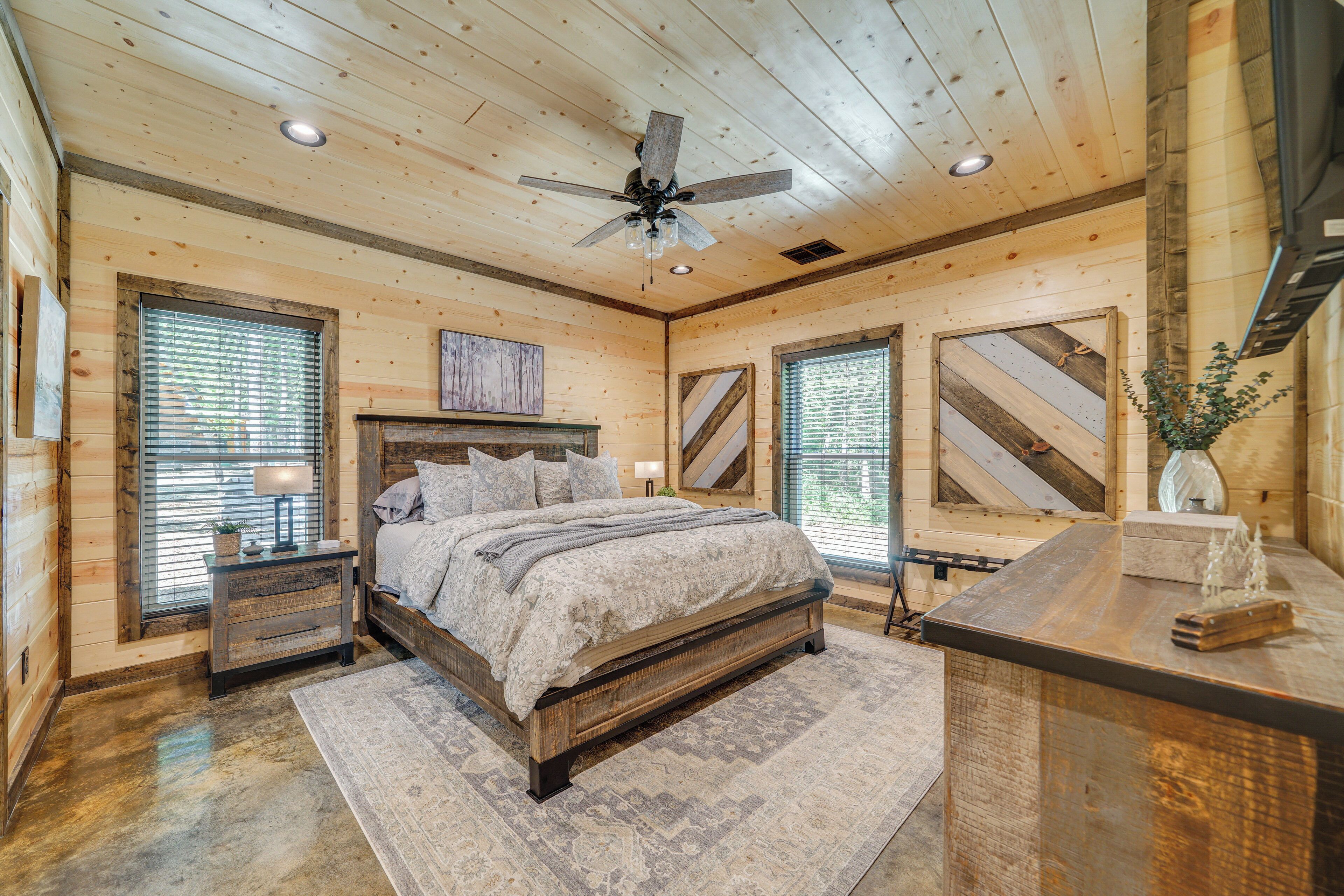A wooden cabin bedroom with a bed, nightstands, a desk, and a ceiling fan.