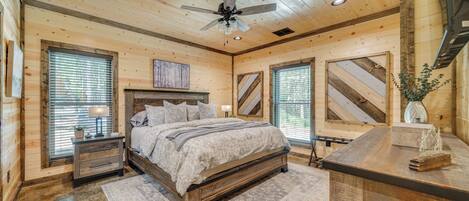 Een slaapkamer in een houten chalet, met een bed, nachtkastjes, een bureau en een plafondventilator.