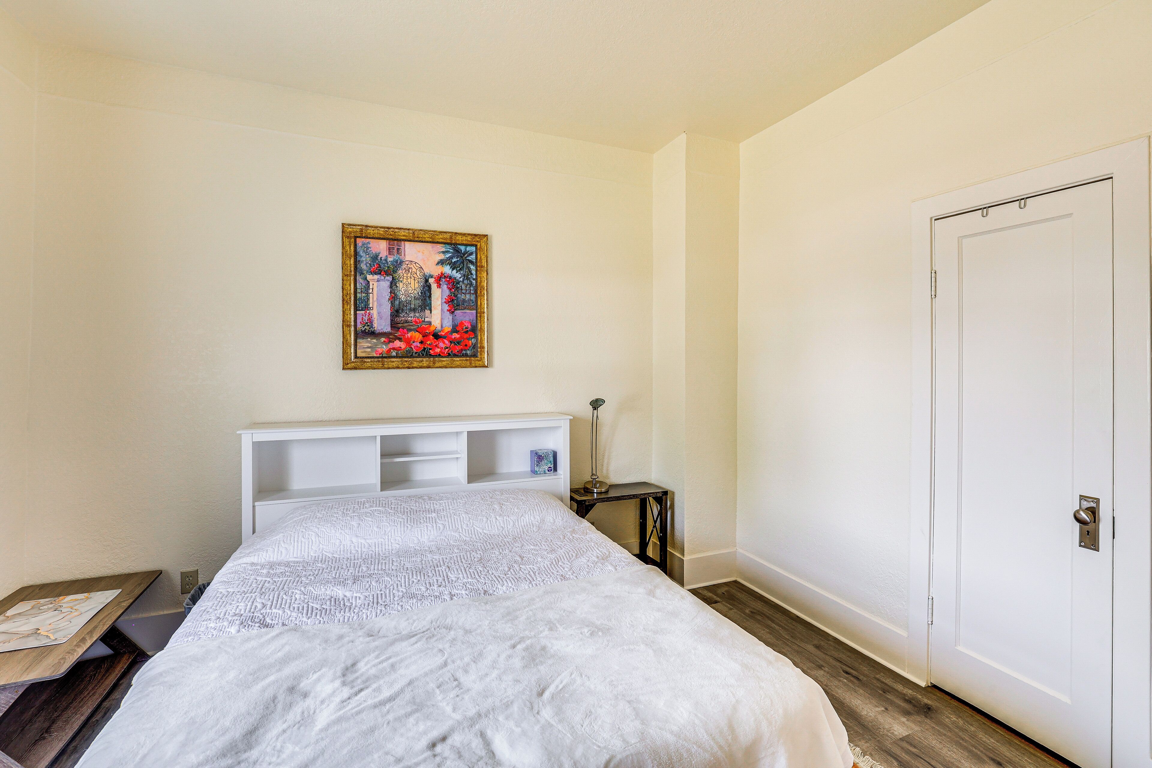 Een slaapkamer met een bed, nachtkastje, schilderij aan de muur en een deur.