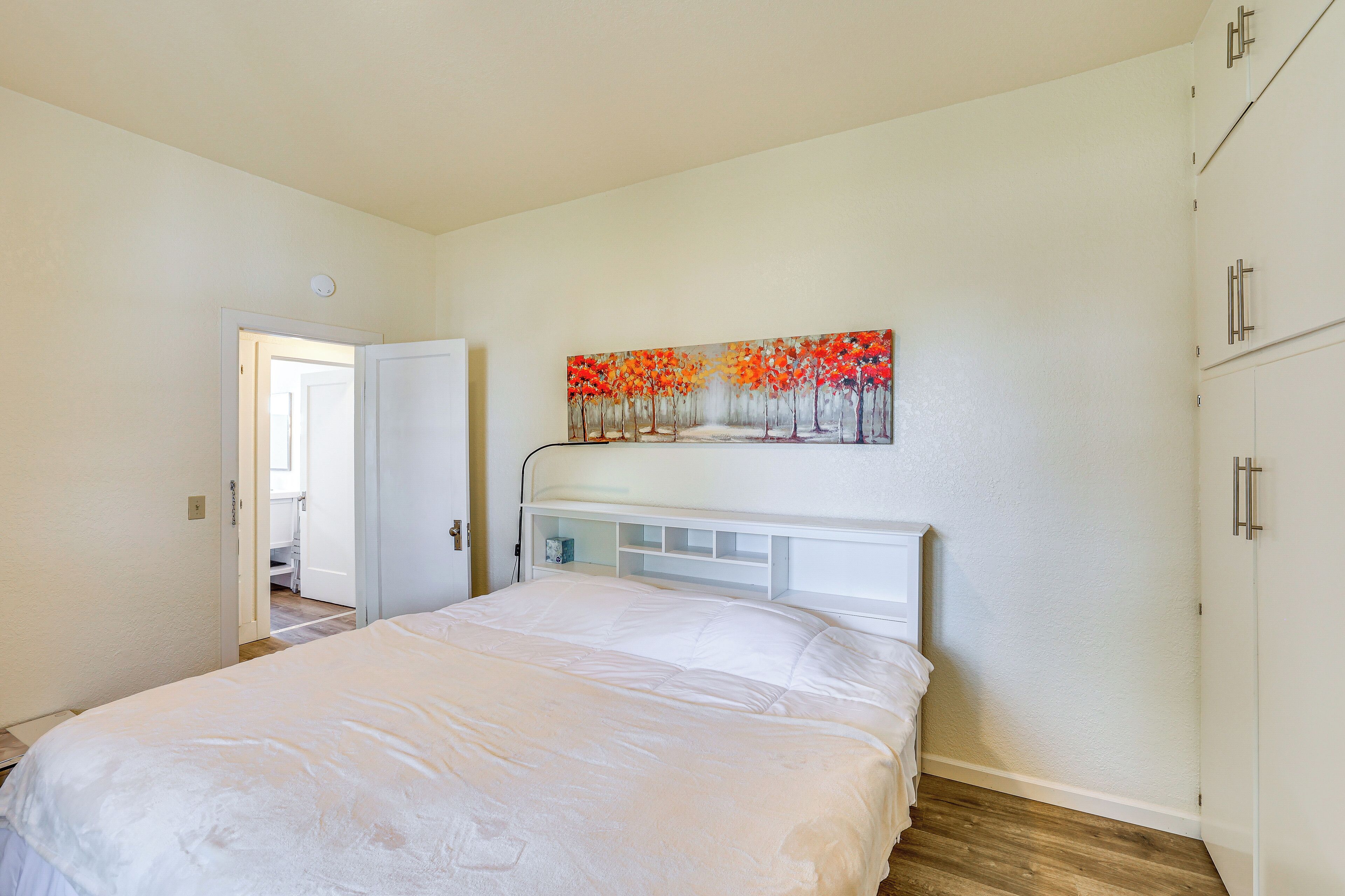 A bedroom with a bed, a painting above it, and a wardrobe.
