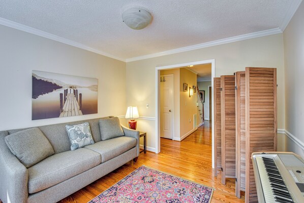 A living room with a sofa, a rug, a keyboard, and a painting on the wall. - Anderson Retreat: Private Dock, Kayaks, Fire Pit! (Anderson)