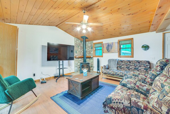 Un salón acogedor con techo de madera, chimenea, televisor y sofá estampado.