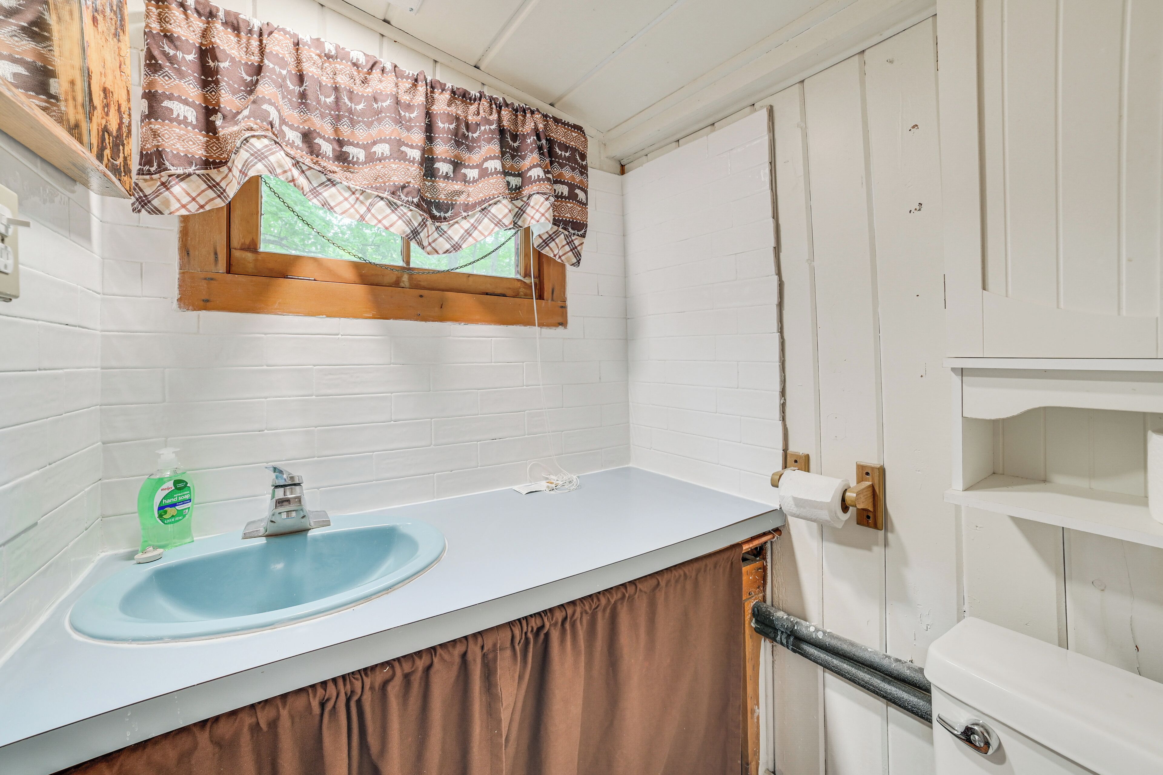 A bathroom with a white sink, a window with patterned curtains, and a white toilet.