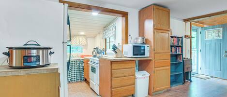A compact kitchen with a stove, microwave, and a crockpot on the counter.