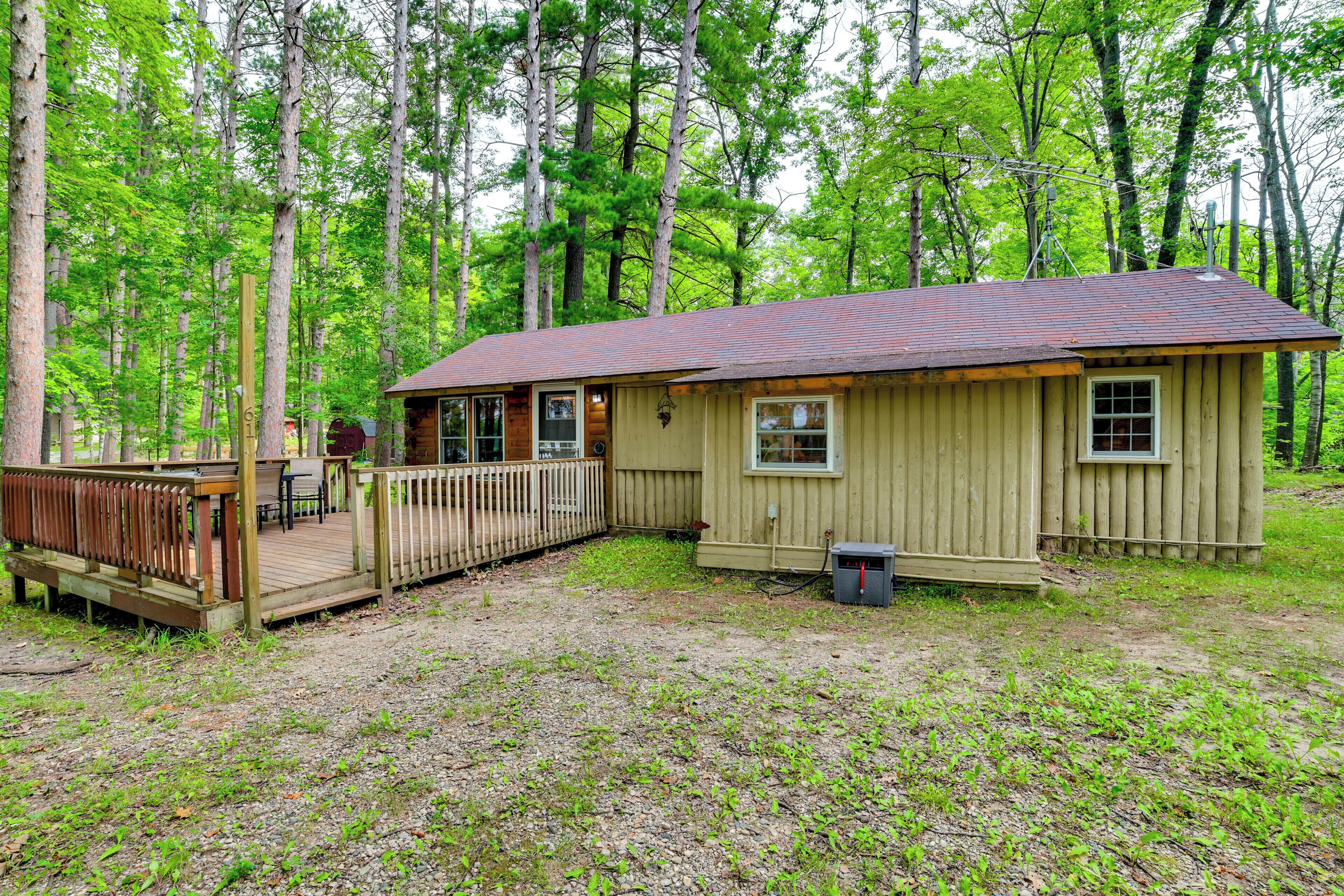 A small wooden cabin with a deck, surrounded by trees.