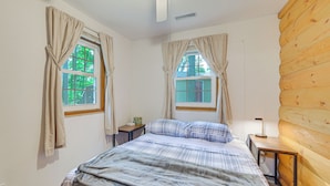 Un dormitorio con una cama, dos ventanas con cortinas, un ventilador de techo y una pared de madera.