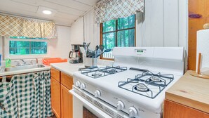 Una cocina con estufa blanca, armarios de madera, un lavamanos y un ventanal con vista a árboles.