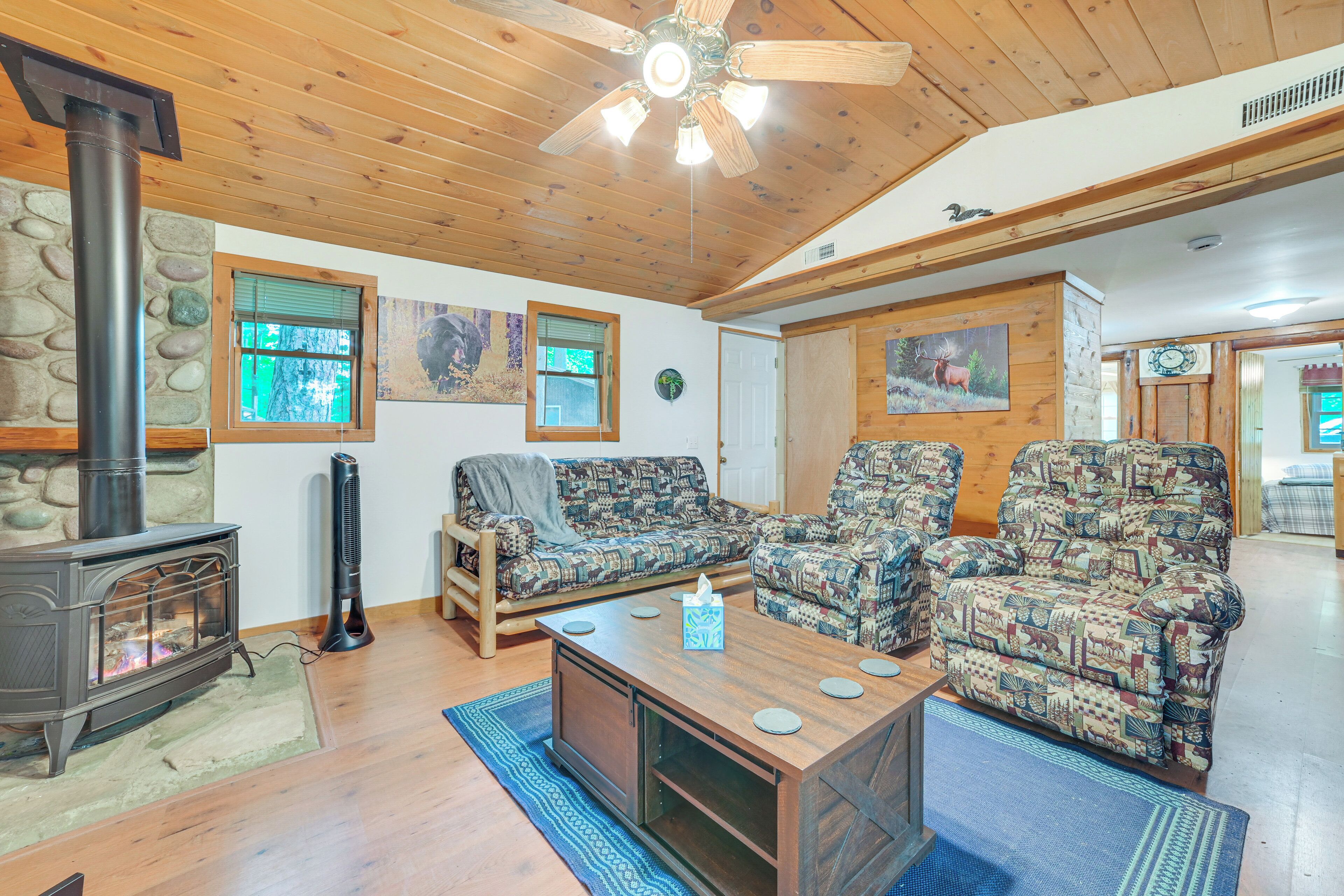 A cozy living room with a wood stove, patterned sofas, a coffee table, and a ceiling fan.