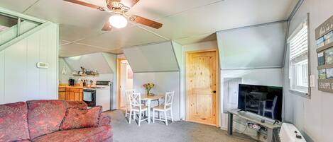 A compact living space with a kitchenette, a sofa, a dining table with chairs, a ceiling fan, and a television.