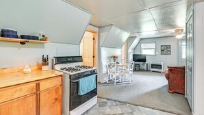 Une cuisine compacte équipée d’une cuisinière, d’un four et de meubles en bois. On y trouve un coin repas avec une table et des chaises, ainsi qu’un canapé rouge à motifs.