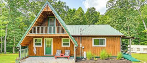 A wooden cabin with a green roof, a balcony, and a small porch with two chairs.