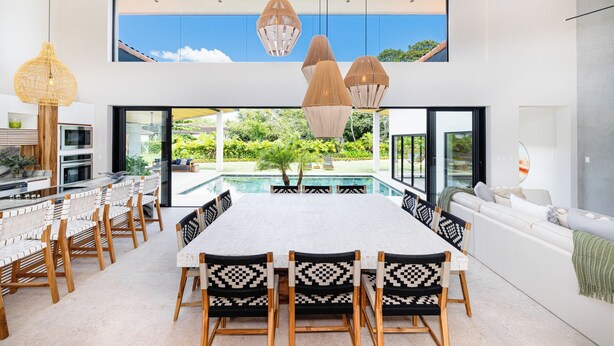 A modern dining area with a pool view, wooden chairs, and a large table. - Modern villa at exclusive Hacienda Pinilla 5min from beach/golf & beach club (Tamarindo)