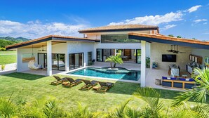 A modern house with a swimming pool, outdoor seating, and a large TV screen. - Modern villa at exclusive Hacienda Pinilla 5min from beach/golf & beach club (Tamarindo)
