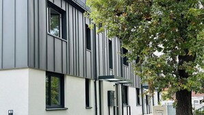 Un bâtiment moderne doté d’un toit plat, de grandes fenêtres et d’un arbre au premier plan.