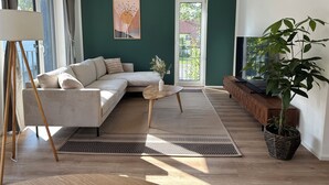 Un salon moderne avec un canapé d’angle, une table basse, un téléviseur et une grande plante en pot.