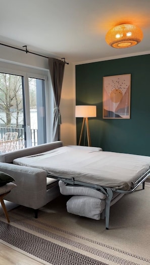 Um quarto com cama, luminária, janela com cortinas e um quadro na parede.