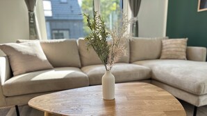 Un salon avec une table basse en bois, un canapé beige et un vase blanc contenant des plantes séchées.