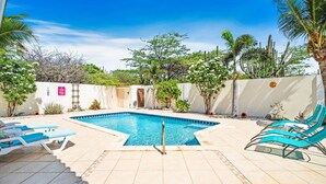 Una piscina con lettini, circondata da un giardino con piante e alberi.