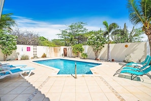 A swimming pool with lounge chairs, surrounded by a garden with various plants and trees. - Private Pool & Patio Haven, 3BR House near Beach (Noord)